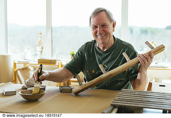 Smiling senior man paining wood in workshop