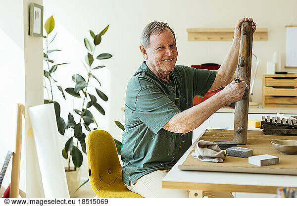Smiling senior man painting wood in workshop
