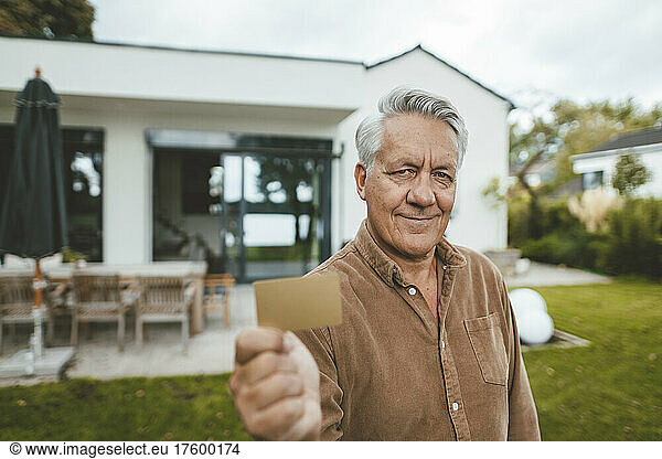 Smiling senior man showing credit card at backyard