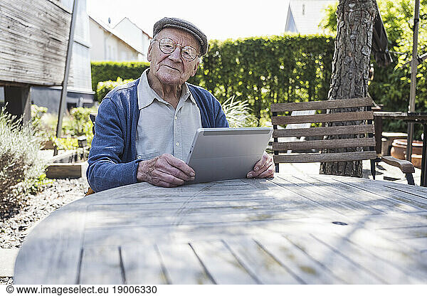 Smiling senior man sitting with tablet PC at table