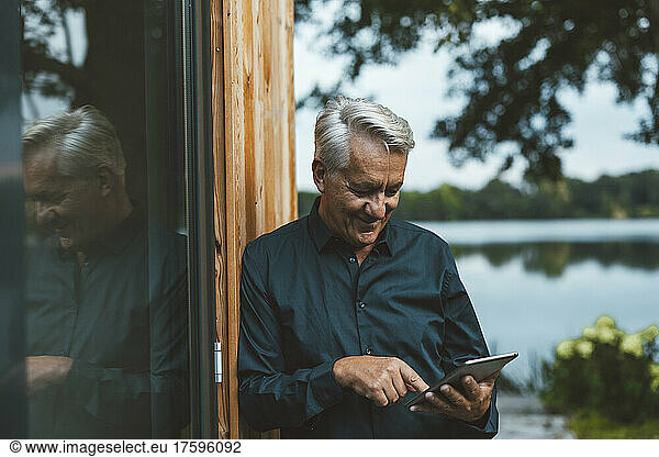 Smiling senior man using tablet PC by glass wall at backyard