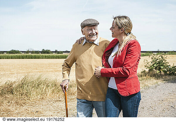 Smiling senior man walking with woman by field on sunny day