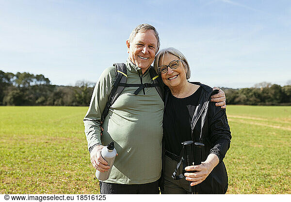 Smiling senior man with arm around woman standing on green landscape