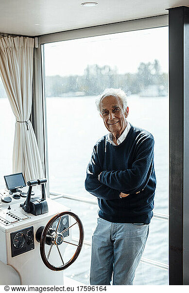 Smiling senior man with arms crossed leaning on window at houseboat