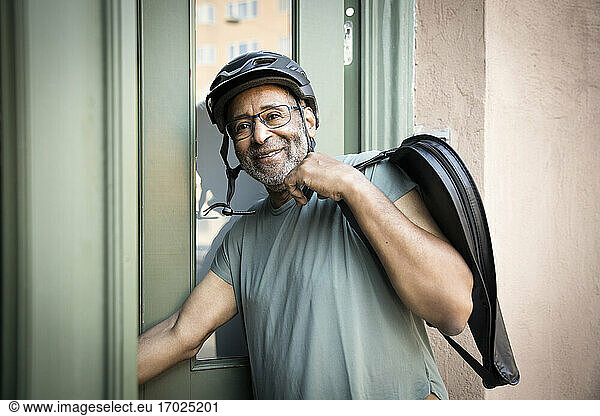 Smiling senior man with bag by doorway outside house