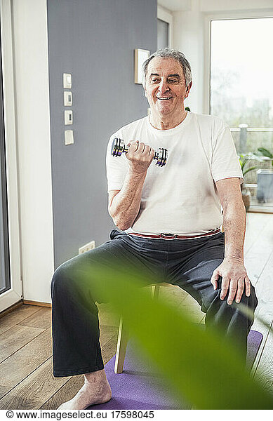 Smiling senior man with dumbbell exercising at home