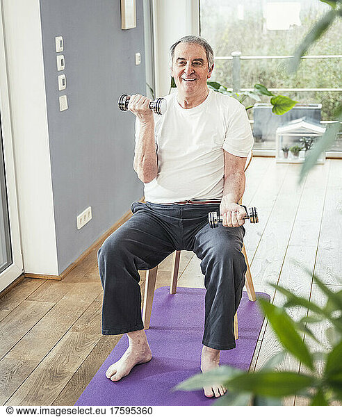 Smiling senior man with dumbbell practicing exercise at home