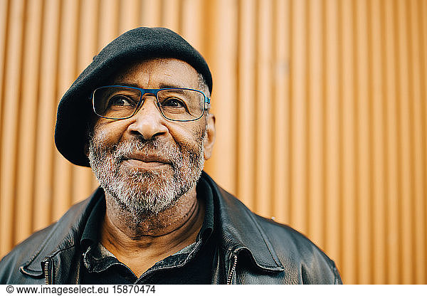 Smiling senior man with eyeglasses against wall
