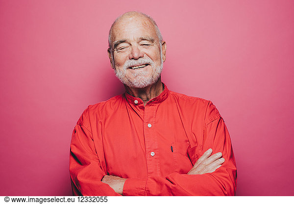 Smiling senior man with eyes closed against pink background