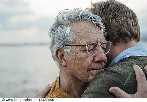 Smiling senior man with gray hair hugging son