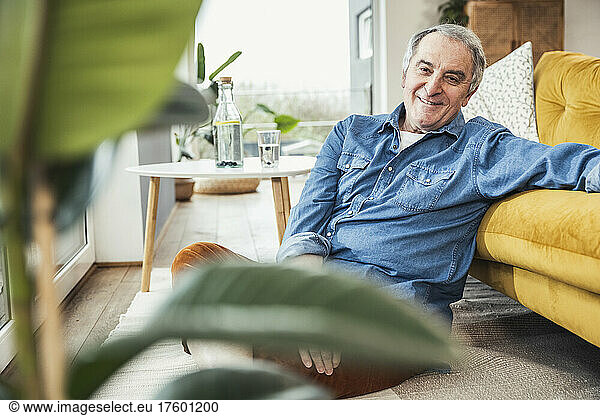 Smiling senior man with gray hair sitting by sofa at home