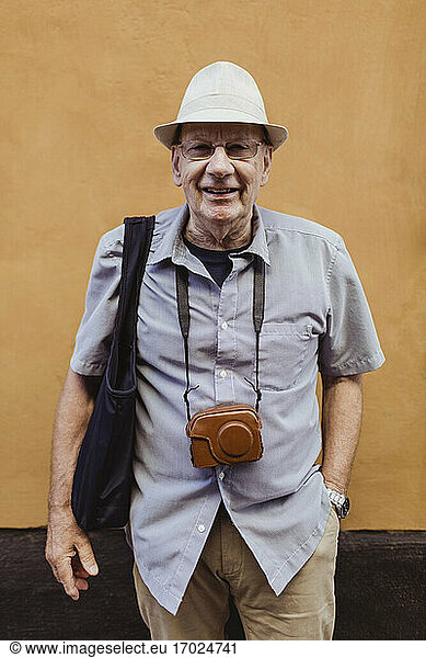 Smiling senior man with hand in pocket against wall