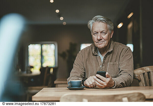Smiling senior man with mobile phone in cafe