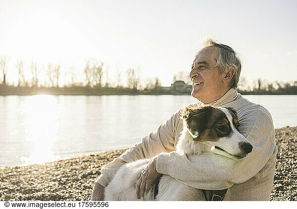Smiling senior man with pet dog at beach on sunny day