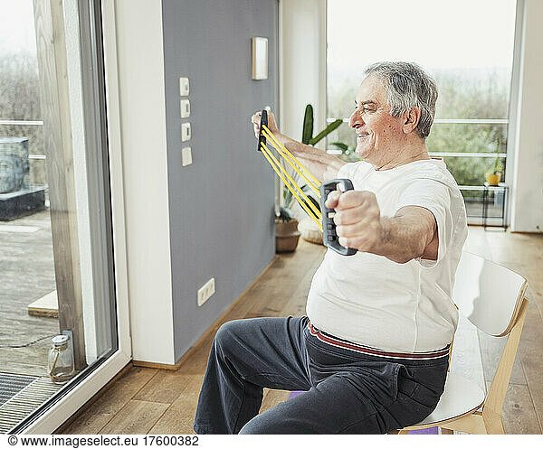 Smiling senior man with resistance band doing stretching exercise at home