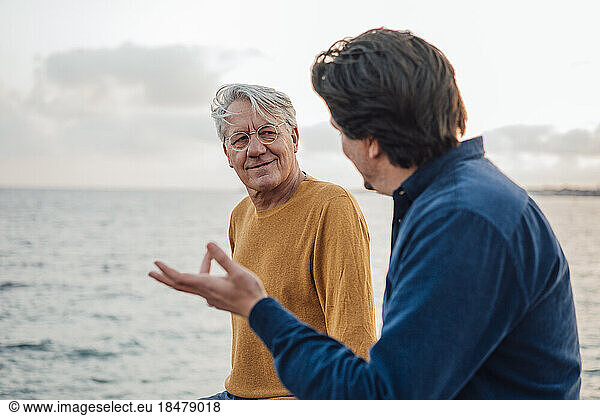 Smiling senior man with son having discussion in front of sea