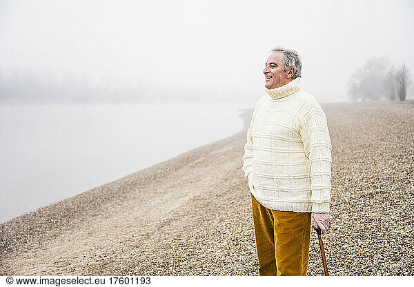 Smiling senior man with walking cane standing at beach