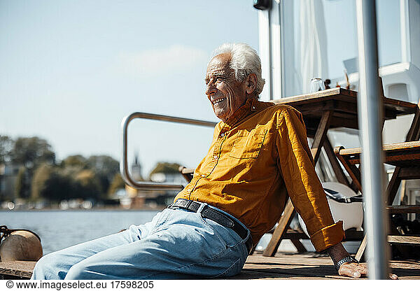 Smiling senior man with white hair relaxing at houseboat on sunny day