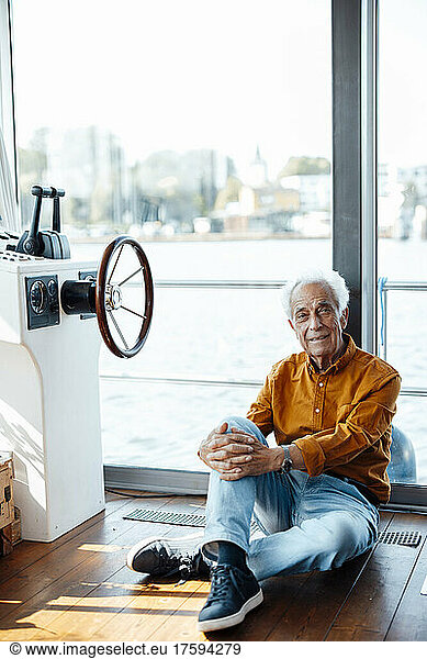 Smiling senior man with white hair sitting by window at houseboat