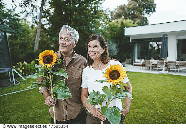 Smiling senior man with woman holding sunflowers at backyard