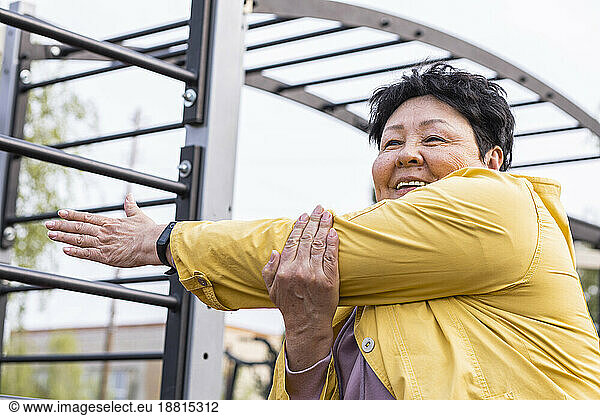 Smiling senior woman doing warm up exercise at park