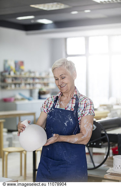 Smiling senior woman holding pottery vase in studio