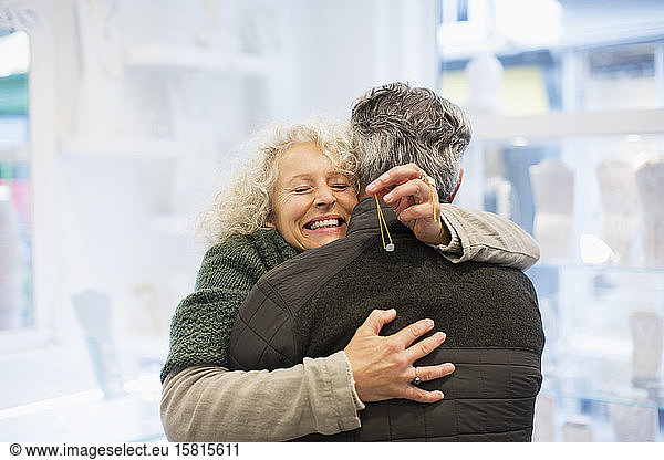 Smiling senior woman hugging husband in jewelry store