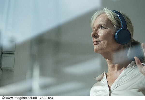 Smiling senior woman listening music through wireless headphones