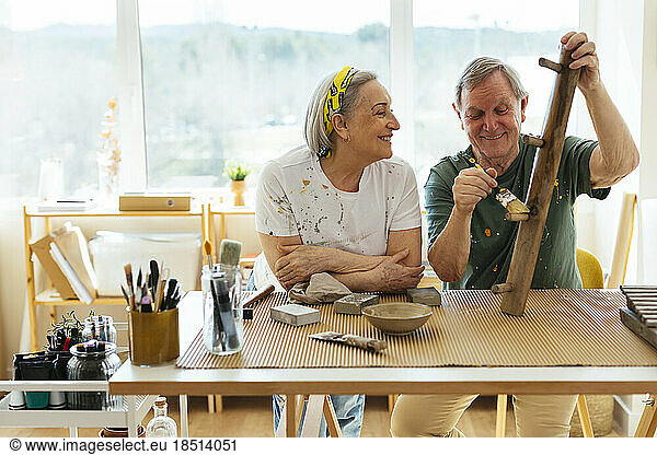 Smiling senior woman looking at man polishing wood in workshop