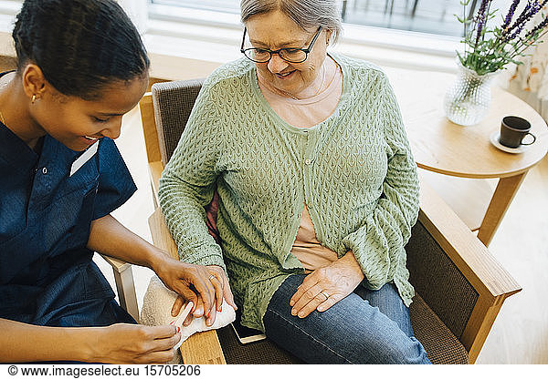 Smiling senior woman looking at young female caretaker filing her nails in retirement home