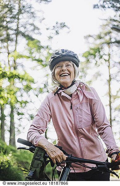 Smiling senior woman looking away while standing with cycle