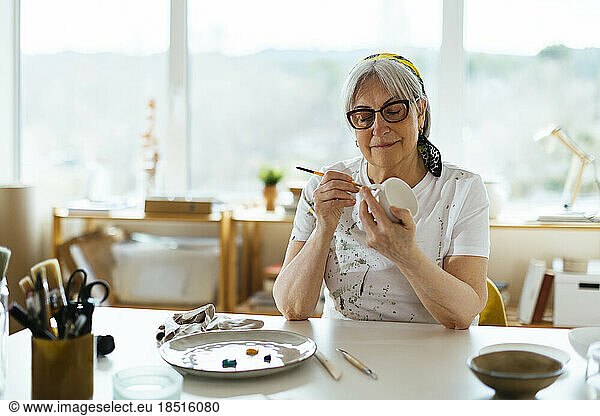Smiling senior woman painting cup at studio