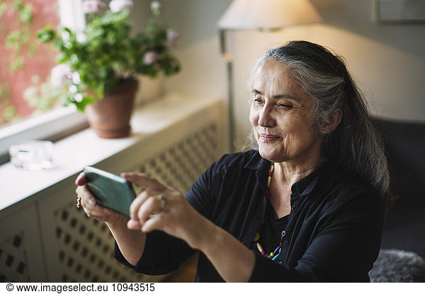 Smiling senior woman photographing through mobile phone