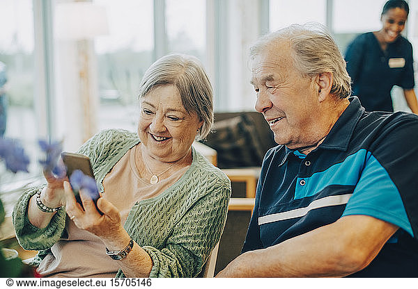 Smiling senior woman sharing smart phone with man while sitting at retirement home
