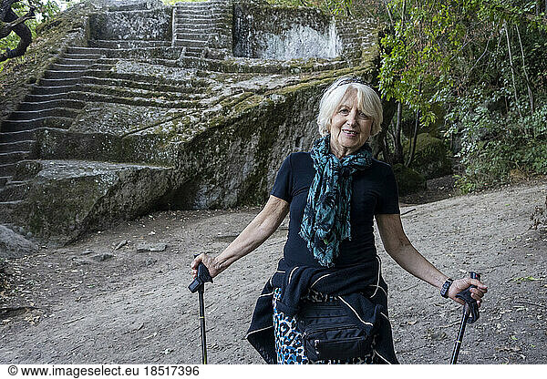 Smiling senior woman standing with walking sticks at Etruscan Pyramid of Bomarzo
