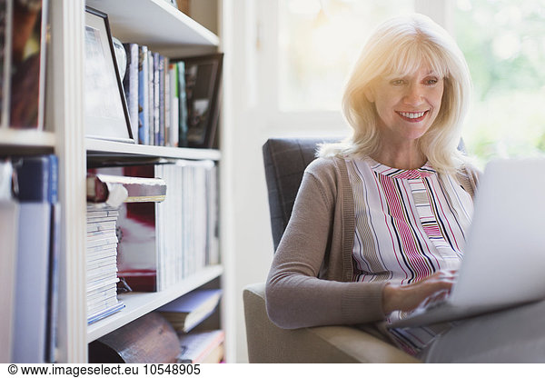 Smiling senior woman using laptop in den
