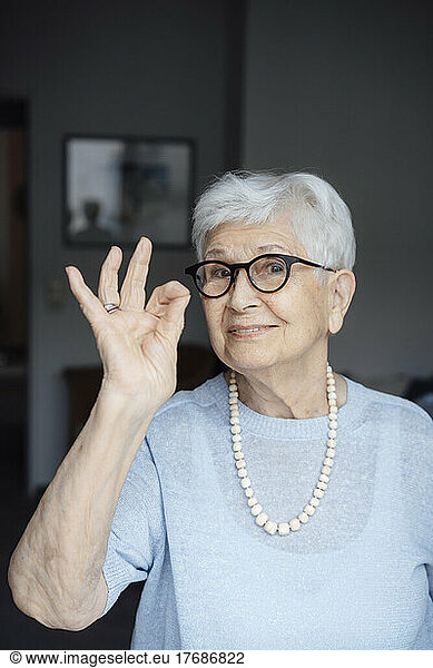 Smiling senior woman wearing eyeglasses showing OK sign gesture