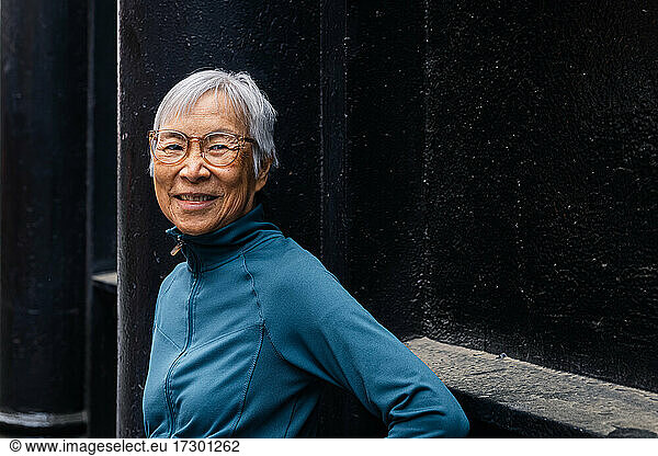 Smiling senior woman wearing eyeglasses standing by black wall