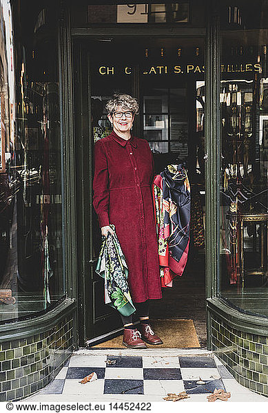 Smiling senior woman wearing glasses and red dress standing front of interior design store  looking at camera.