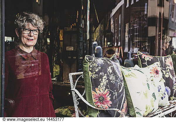 Smiling senior woman wearing glasses and red dress standing in interior design store  looking at camera.