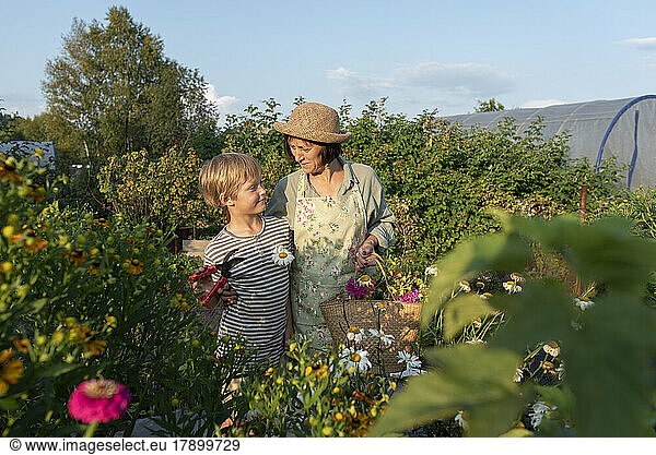 Smiling senior woman wearing hat standing with grandson in garden
