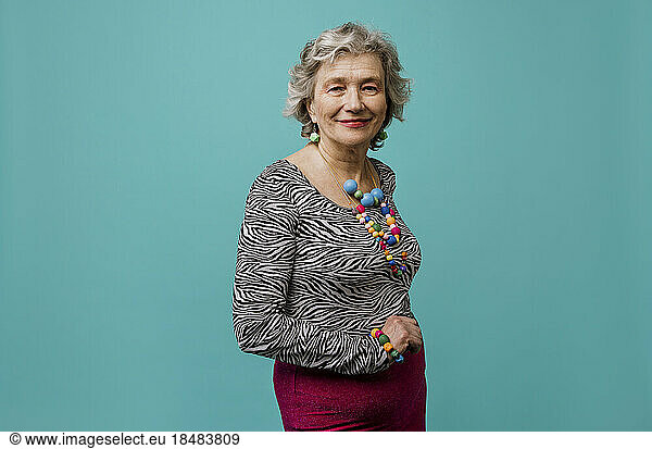 Smiling senior woman wearing multi colored jewelry against turquoise background