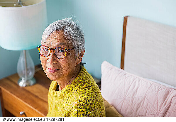 Smiling senior woman wearing yellow sweater sitting in bedroom at home