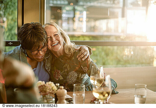 Smiling senior woman with arm around cheerful friend enjoying in restaurant