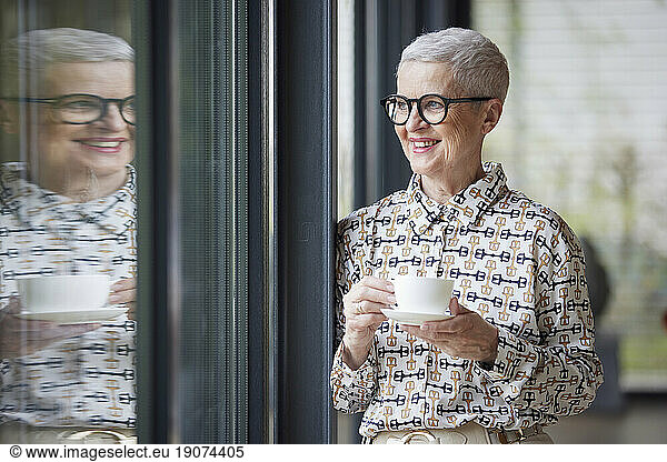 Smiling senior woman with cup of coffee looking out of window
