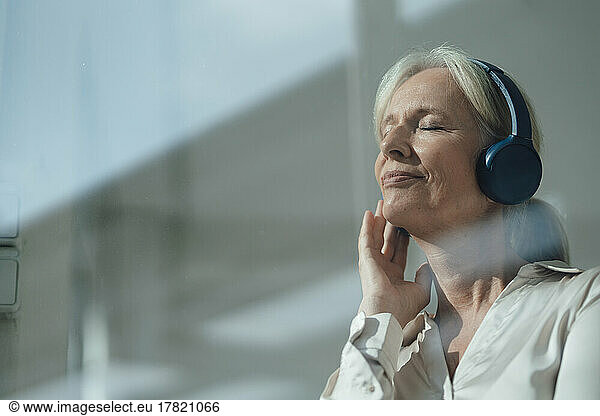 Smiling senior woman with eyes closed listening music through wireless headphones