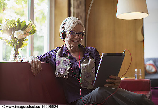 Smiling senior woman with headphones using digital tablet on sofa