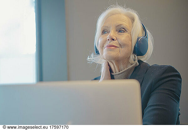 Smiling senior woman with laptop and headphones