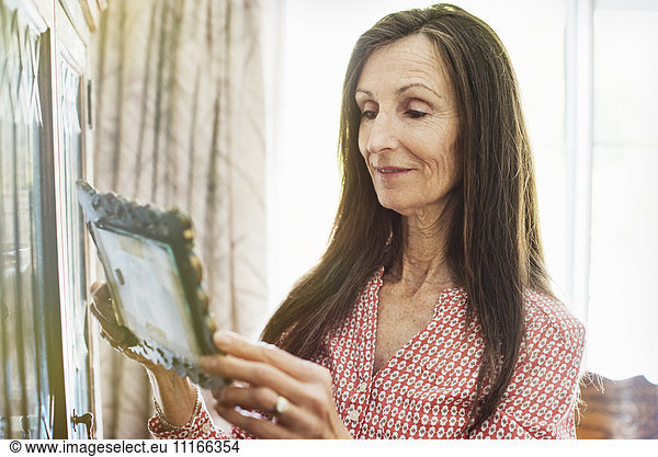 Smiling senior woman with long brown hair holding a picture frame  looking at a picture.