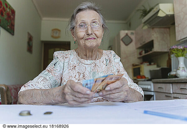 Smiling senior woman with paper currency at home